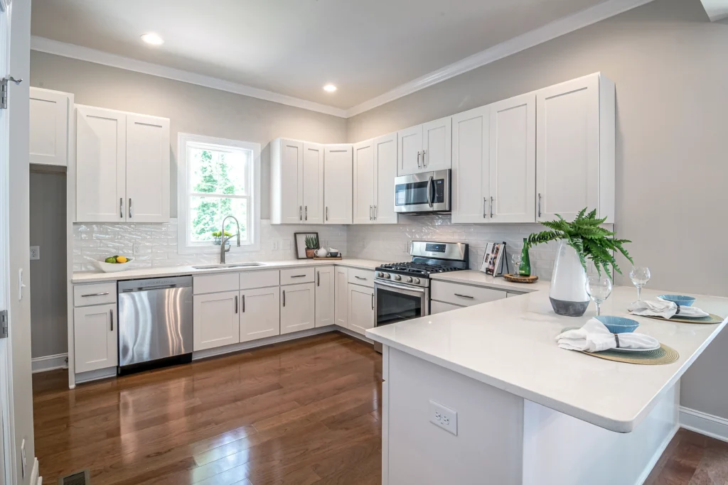 A kitchen with white cabinets and wood floors.