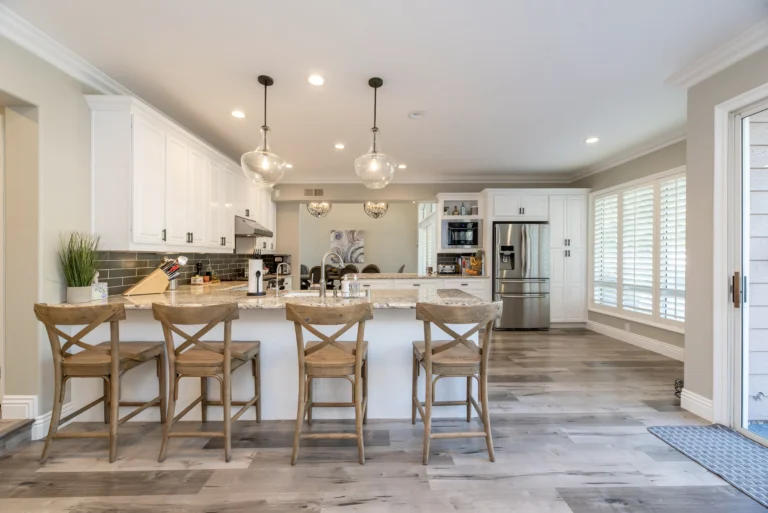 A kitchen with white cabinets and wooden chairs.